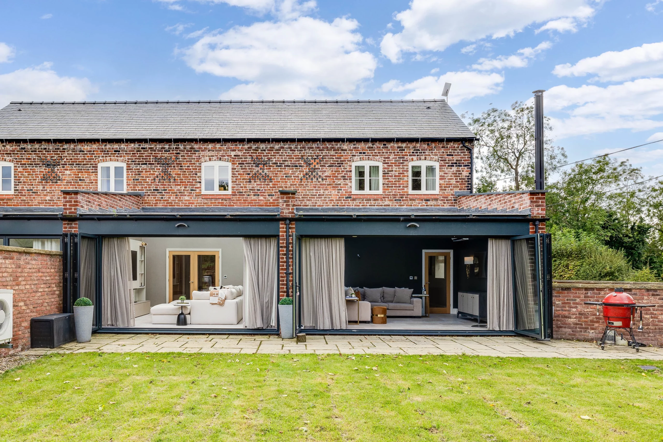 Brick two-storey house with large folding glass doors opening to cosy living rooms and a small lawn in front