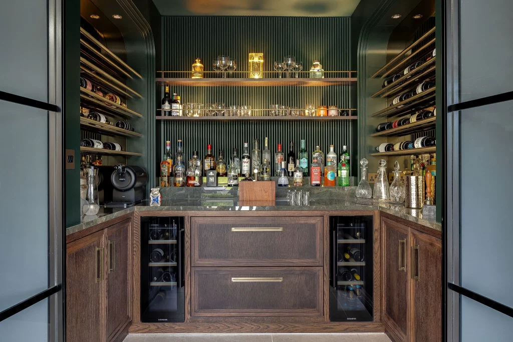 Compact home bar with wooden cabinets, marble counter, bottles and glassware on shelves, and horizontal wine racks each side