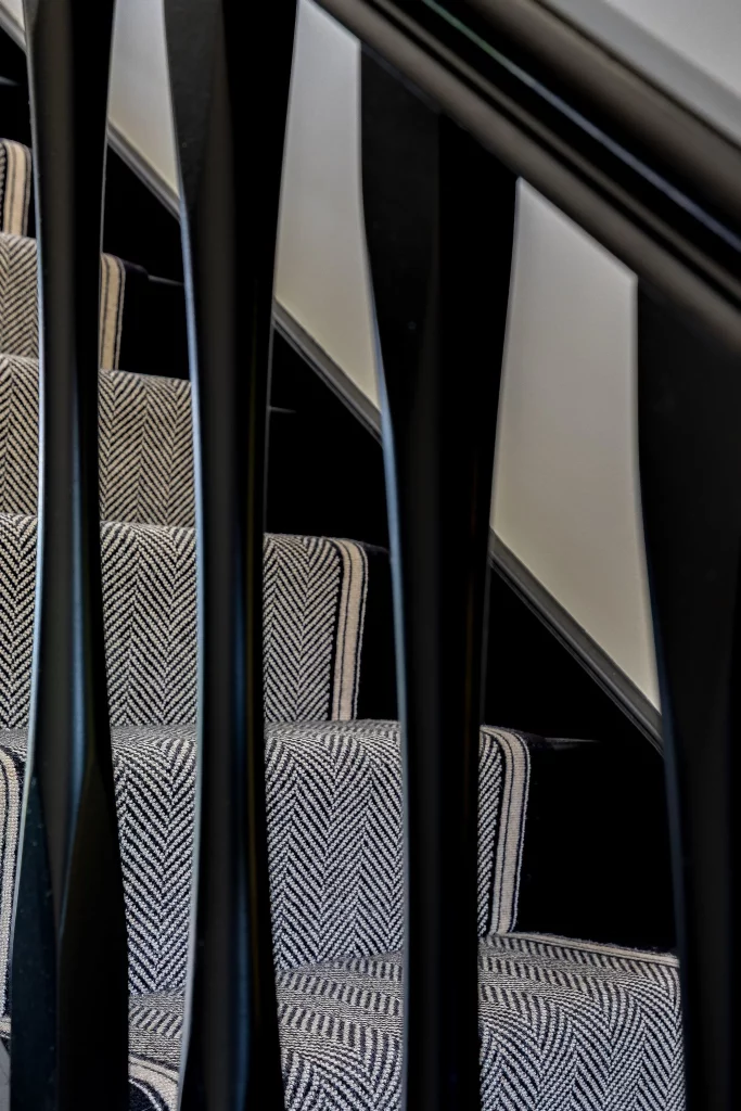 Close-up of carpeted staircase with black vertical balusters and a grey herringbone-pattern stair runner.