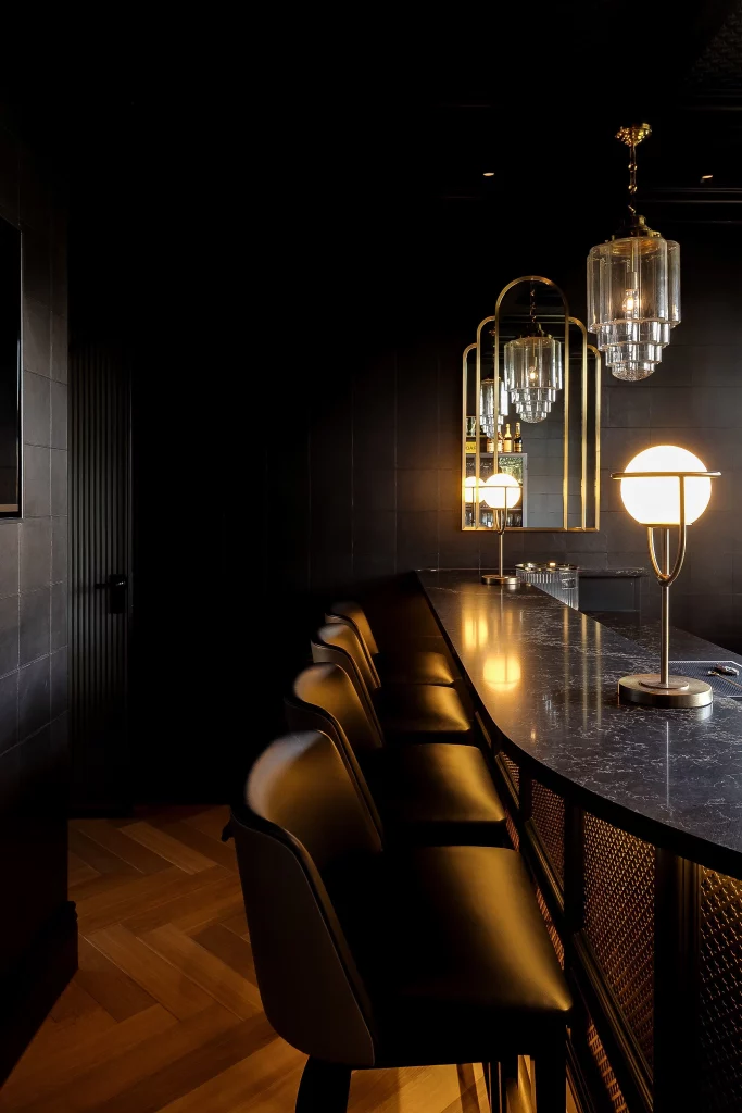 Dark, elegant bar interior with leather bar stools, black marble counter, warm globe lamps and mirrored brass accents.