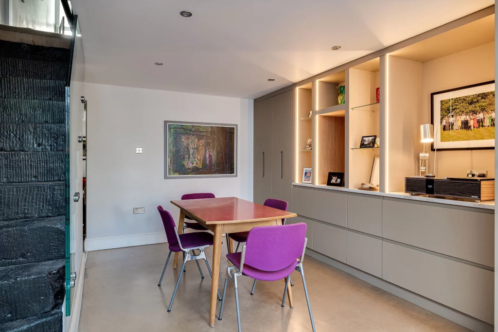 Dining room with a wooden table surrounded by four purple chairs, built-in beige cabinets with lit display shelves and artwork on the walls.