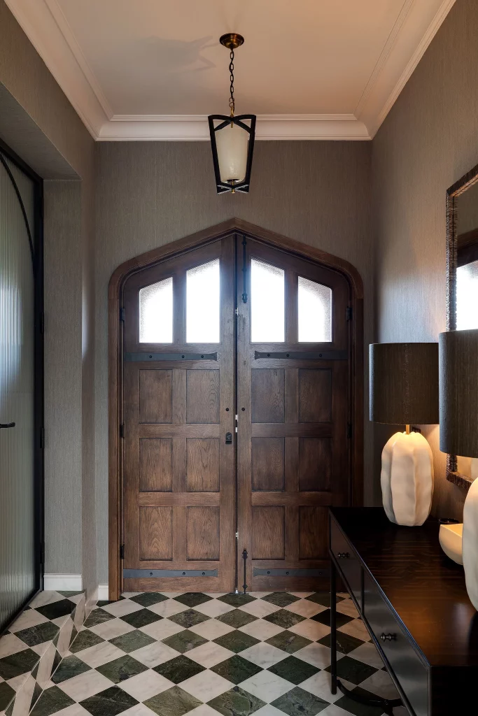 Double wooden arched double doors with frosted upper panes in a muted-entry hall with checkerboard marble floor and console table lamp.