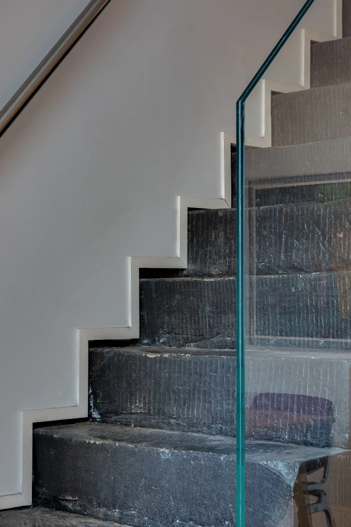 Worn dark stone staircase with stepped white trim, metal handrail and a glass balustrade panel on the right