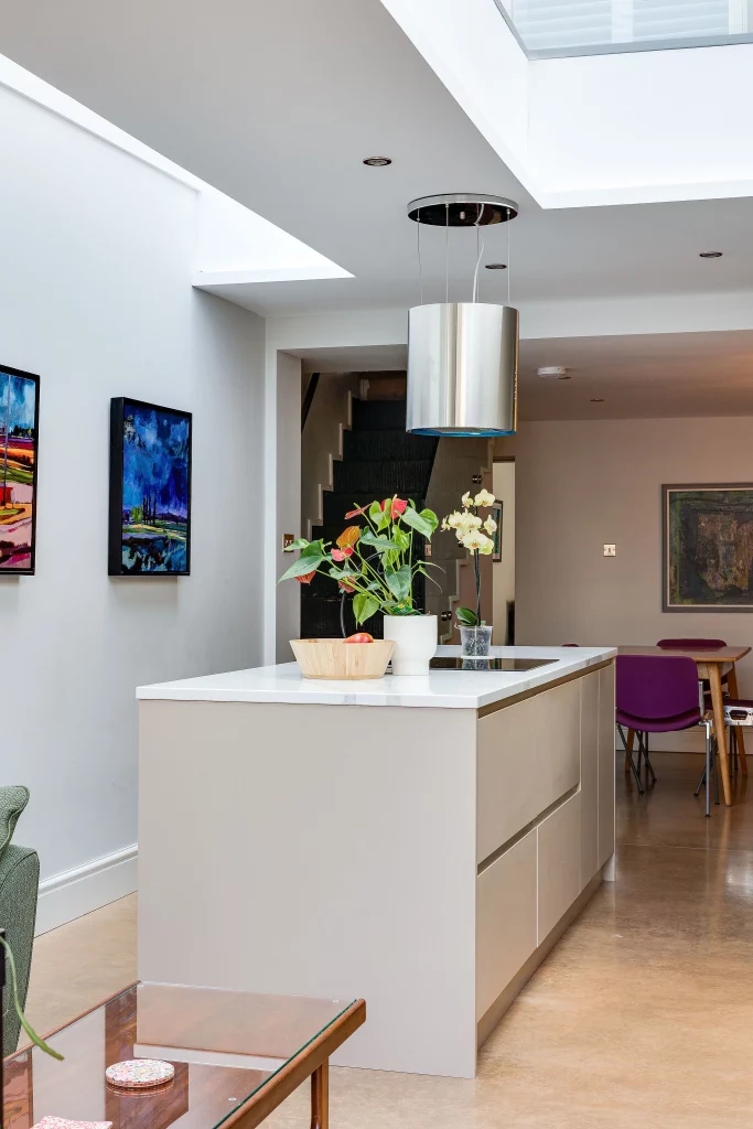 Minimal modern kitchen island with white countertop, potted orchids and anthuriums, pendant light and colourful wall art in open-plan space
