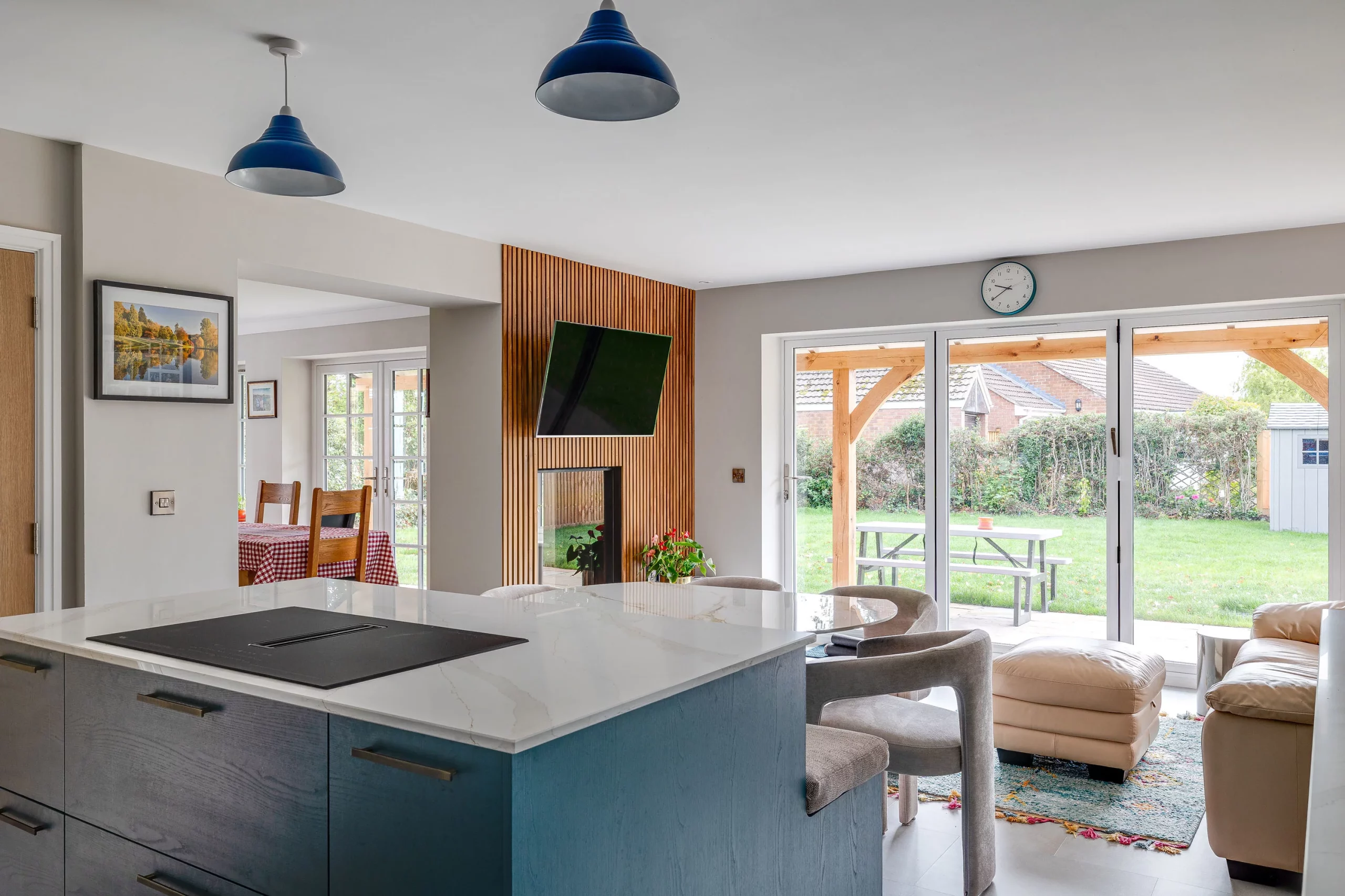 Modern open-plan kitchen and living area with marble island, blue pendant lights, glass doors to garden and cosy seating.