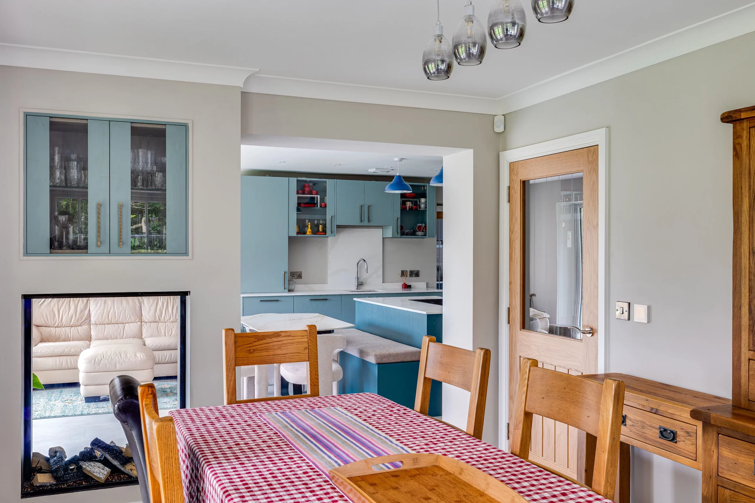 Dining table with red gingham tablecloth and wooden chairs looking into a blue-accent kitchen and adjoining living room