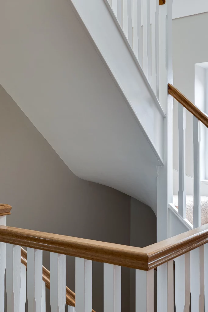 Interior staircase corner with white balusters and wooden handrail against pale grey walls