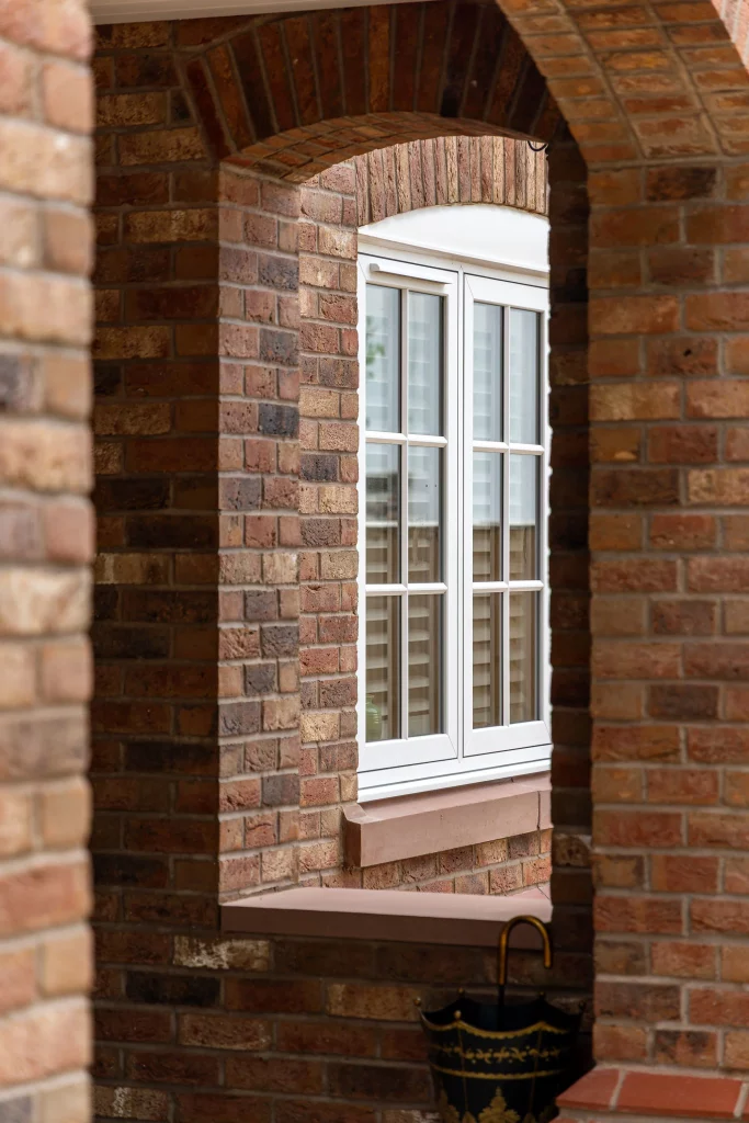 Arched red-brick porch framing a white multi-pane window with shutters and a decorative umbrella stand below.