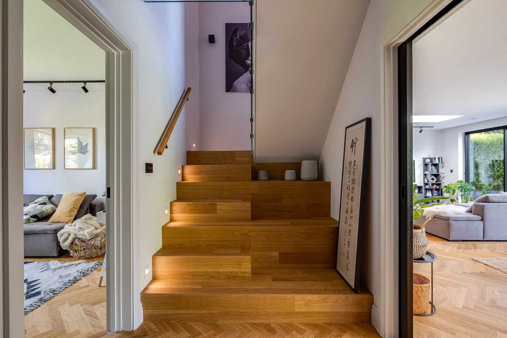 Modern wooden staircase with built-in step lights and a glass balustrade, flanked by cozy living rooms on either side.