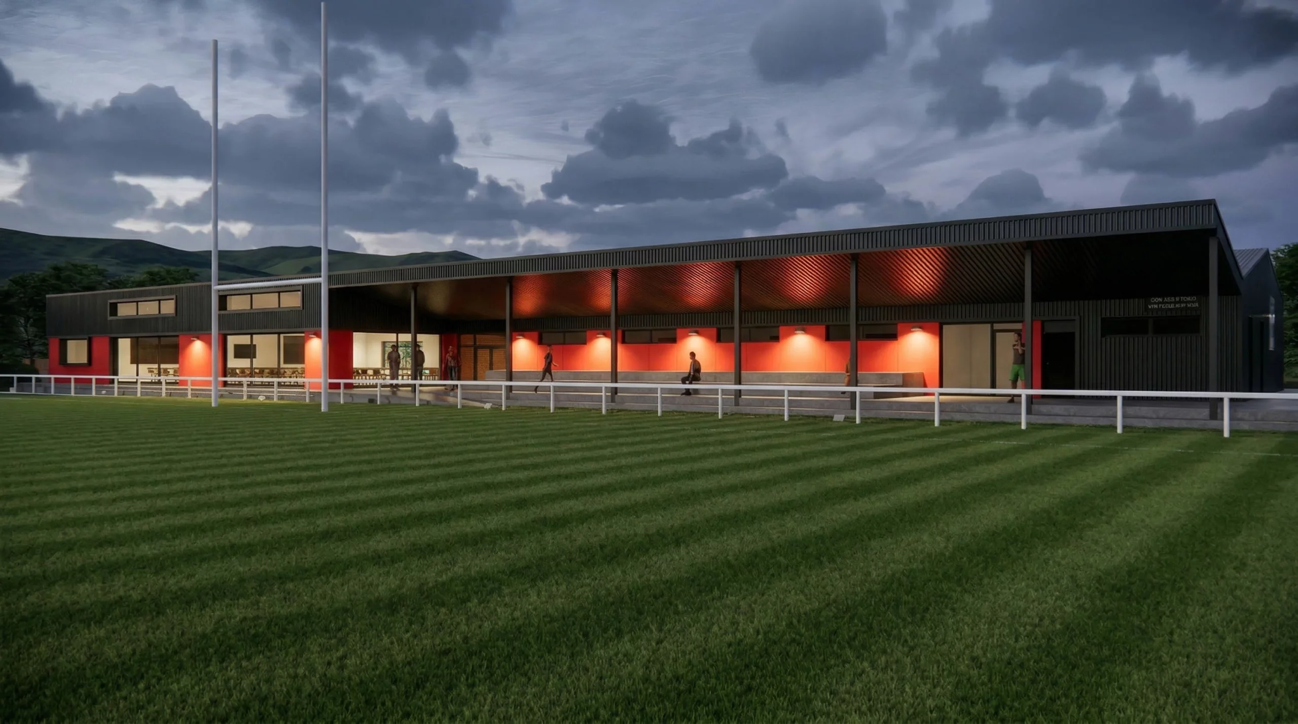 Modern black-and-red sports pavilion with covered spectator seating lit by warm wall lights beside a striped grass field