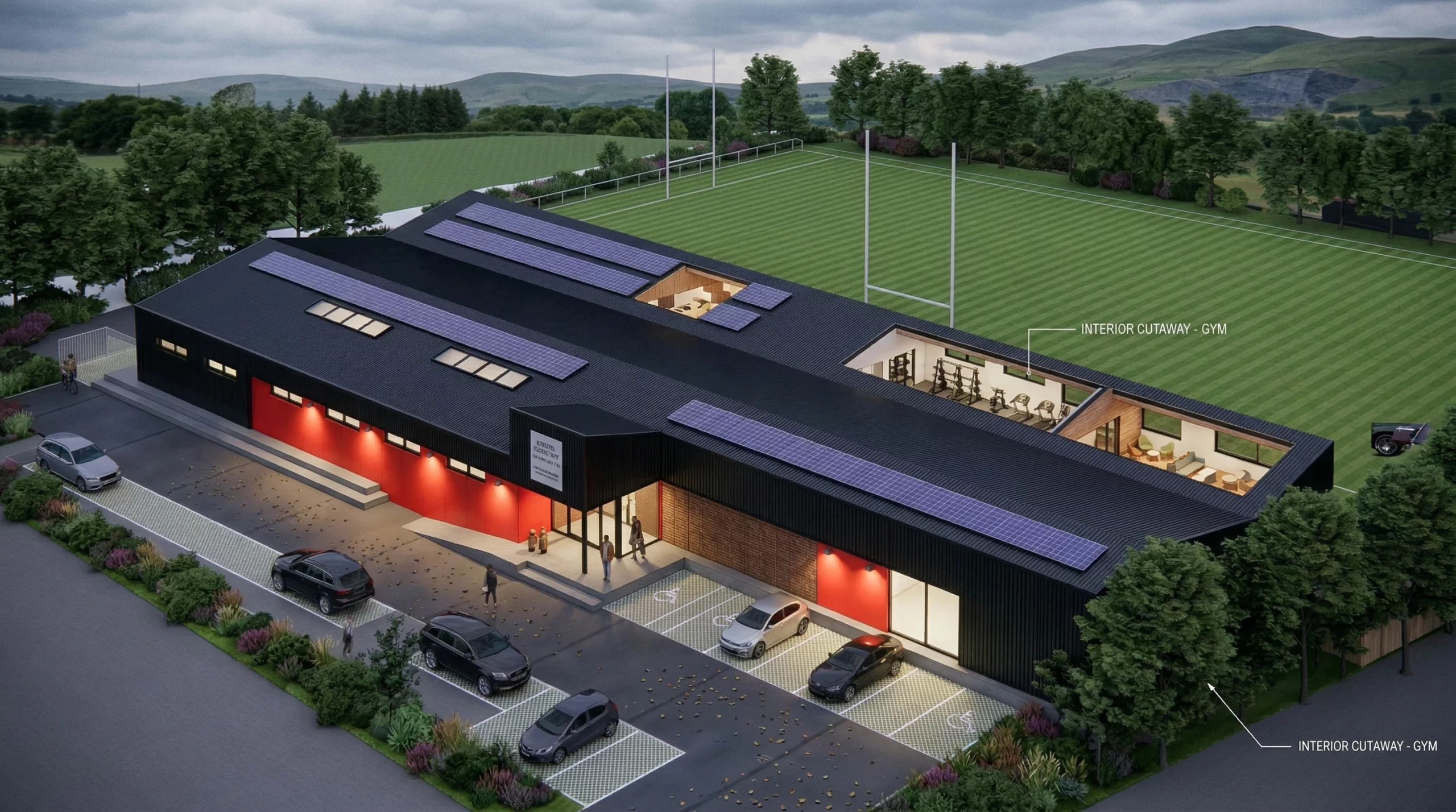 Aerial view of a modern sports centre with solar panels on the roof, parking bays, and a striped rugby pitch beside it.