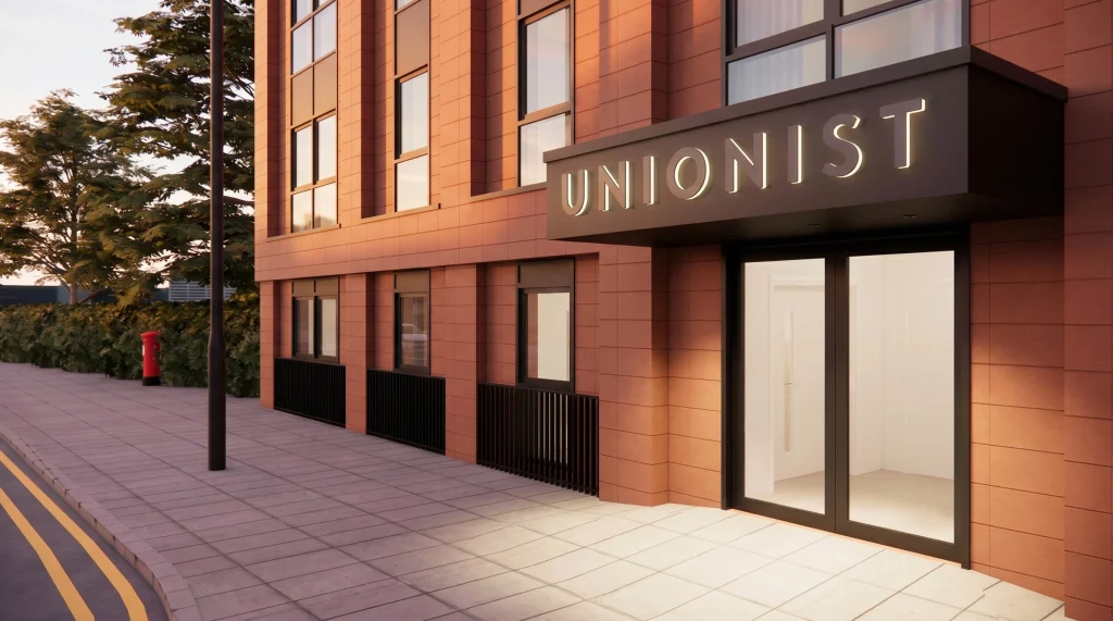 Red-brick modern building entrance with illuminated "UNIONIST" sign above glass doors and a tree-lined pavement with a red post box.