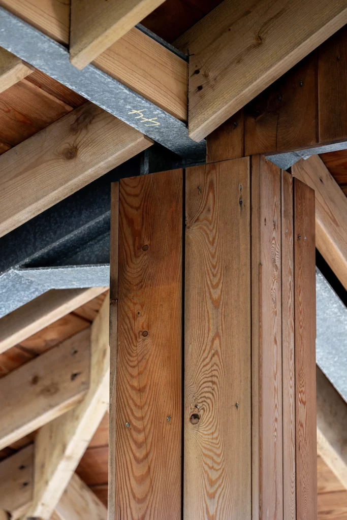 Close-up of wooden beams and planks forming a roof support with visible grain, knots and metal brackets.