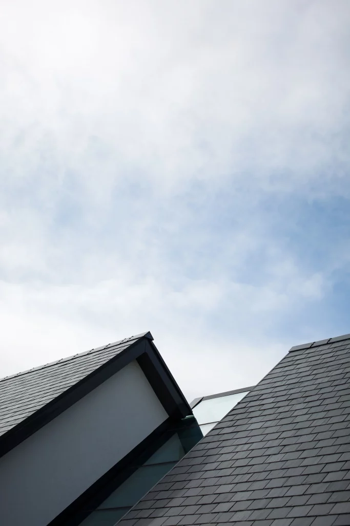 Angled view of two dark slate-roofed gables with white facades against a cloudy blue sky.