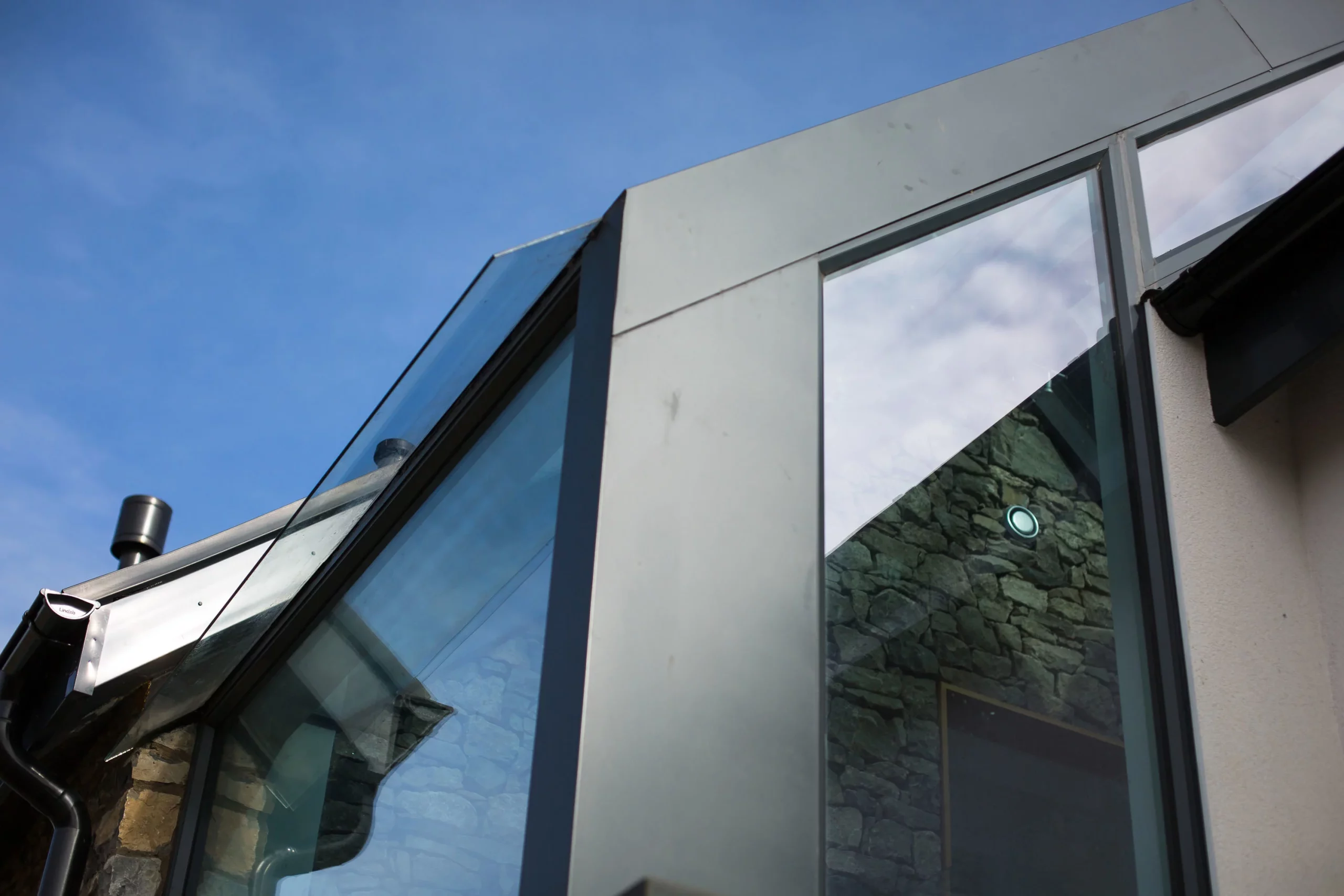 Modern building corner with large reflective glass panels, metal framing and a stone interior wall visible through the window