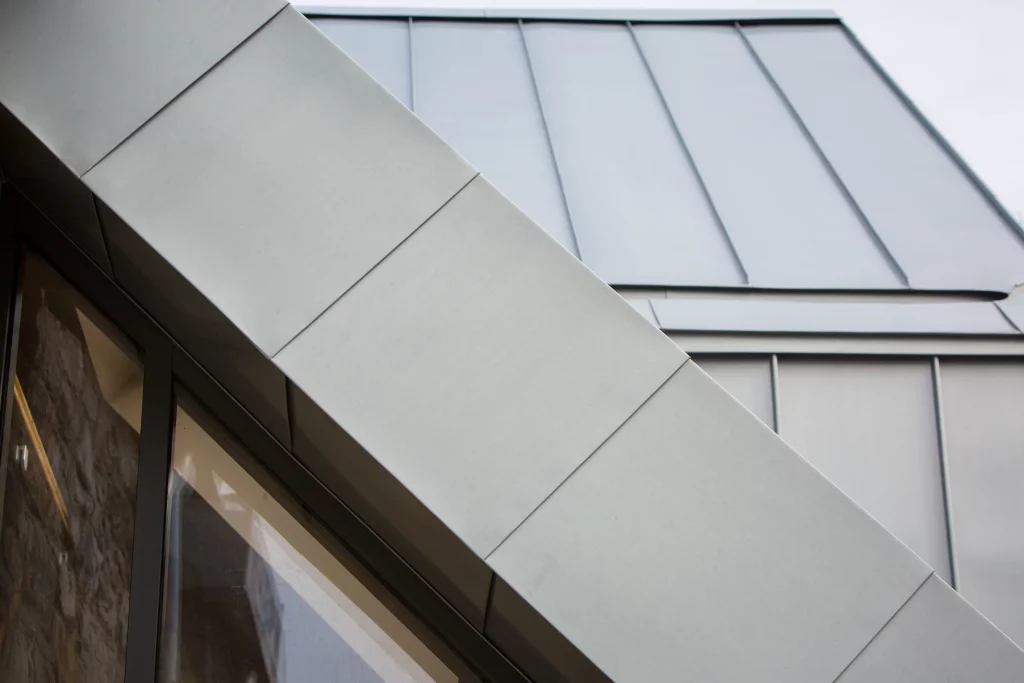 Diagonal close-up of a modern metal-clad building corner with folded panels and a glass window beneath