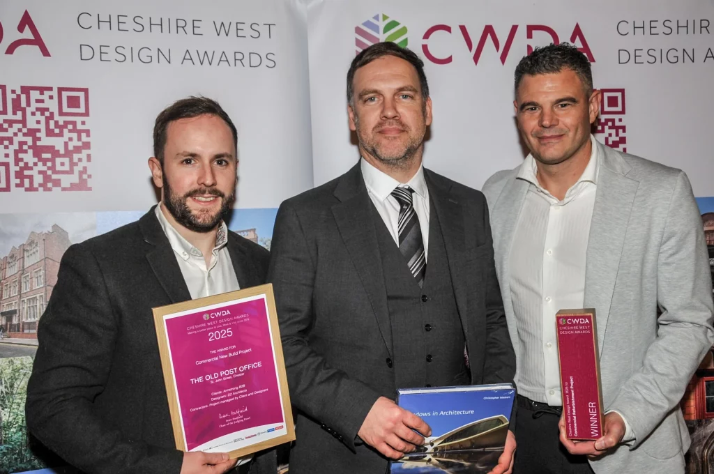 Three men in suits standing side by side at an awards backdrop, the left man holding a framed 2025 Cheshire West Design Awards certificate and the right man holding a red winner trophy.
