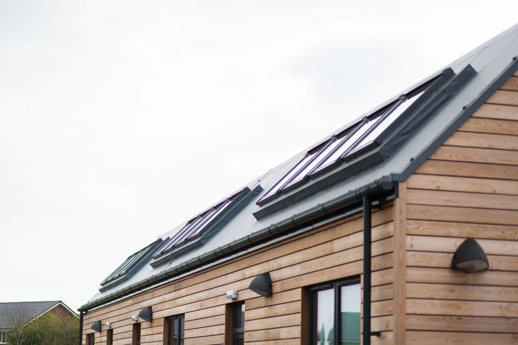 Row of modern wooden houses with sloped metal roofs and multiple roof windows under an overcast sky