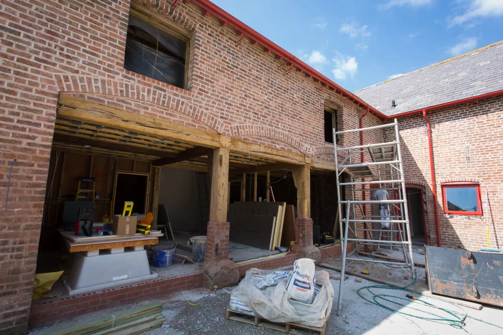 Exposed brick courtyard under renovation with wooden beams, scaffolding, building materials and sacks of cement on a pallet