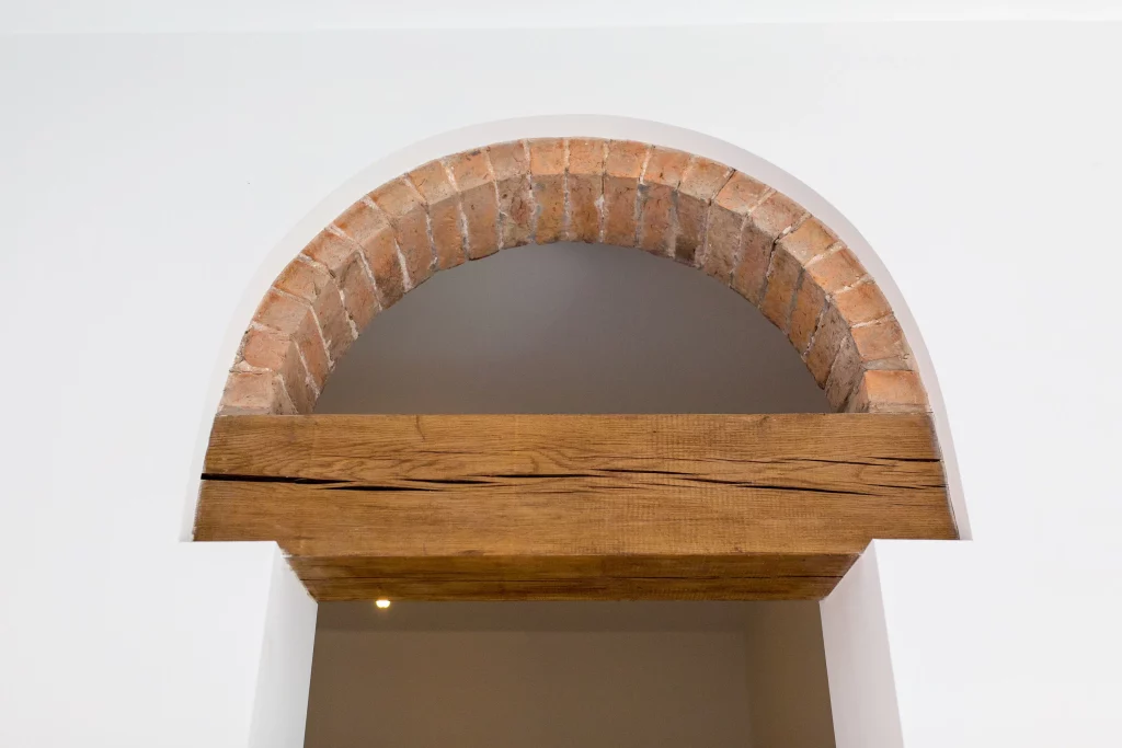 Arched brick doorway set in white plaster with a rough wooden lintel across the opening