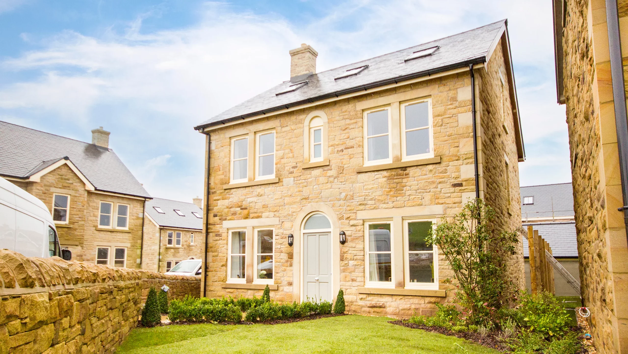 Two-storey sandstone house with slate roof, central pale blue door, symmetrical windows and small front lawn bordered by a low stone wall