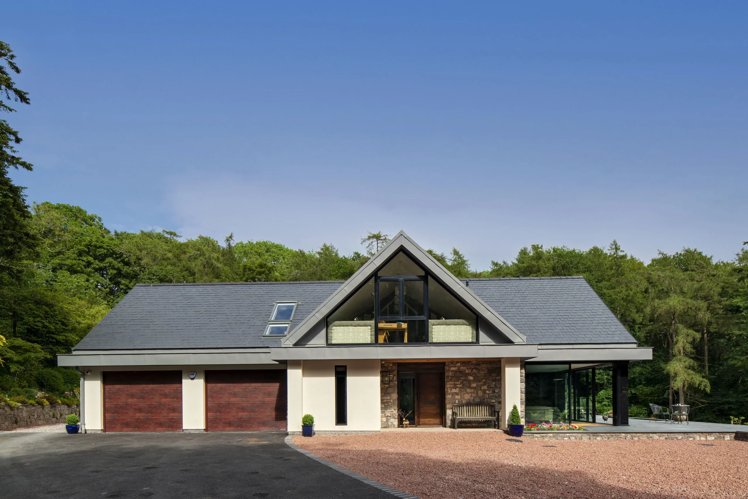 Contemporary two-storey house with A-frame central window, slate roof, double wooden garage doors and surrounding trees