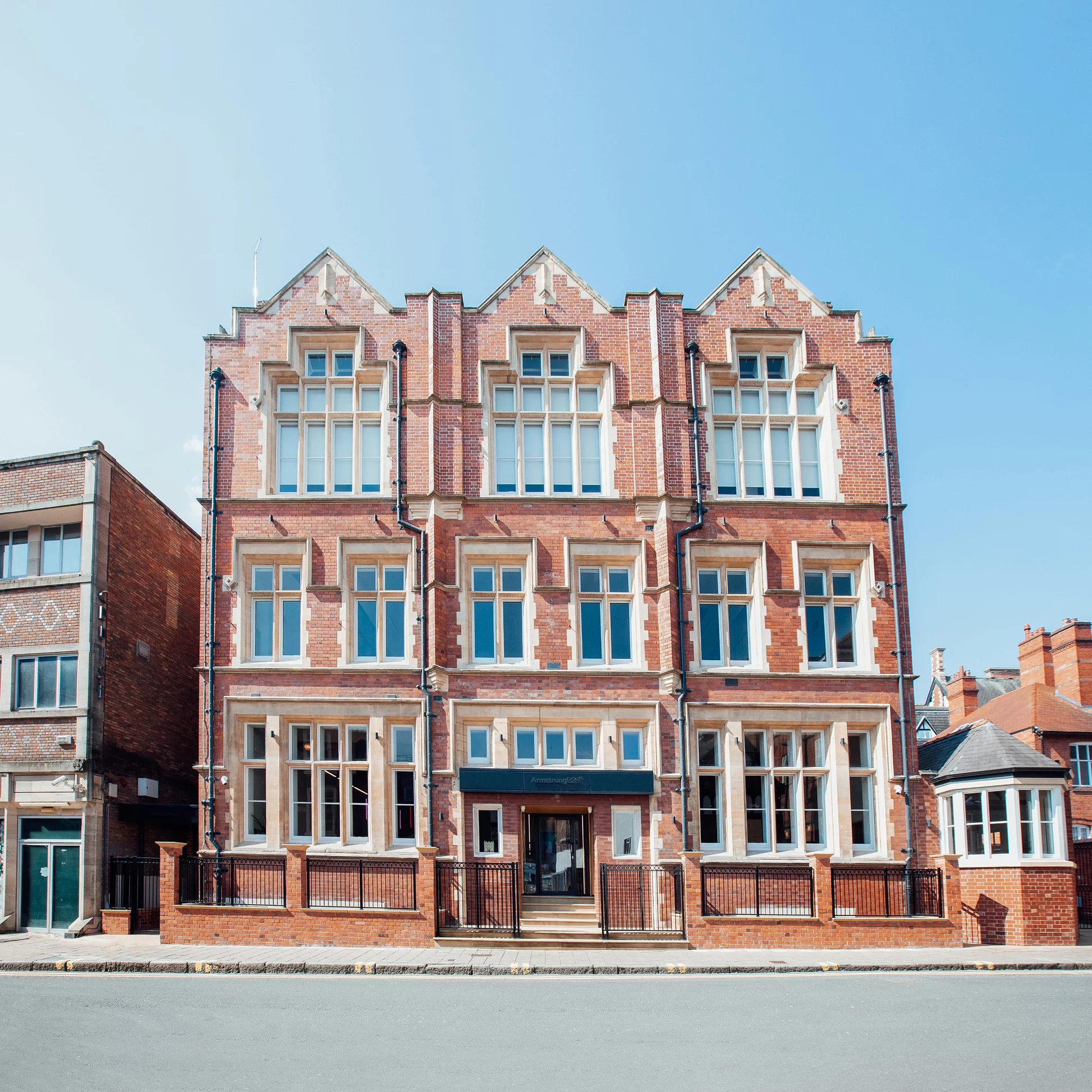 Red-brick Victorian-style building with tall multi-pane windows, decorative gables and a small entrance with black railings
