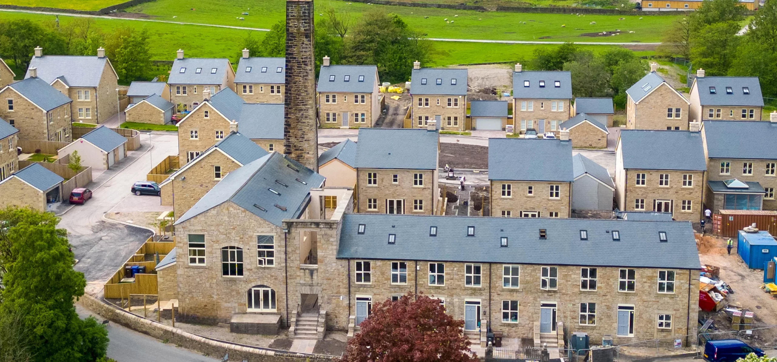 New stone-built housing development with slate roofs clustered around a tall brick chimney in a green rural setting