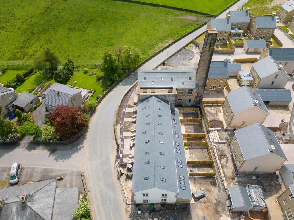 Aerial view of a row of newly built terrace houses and backyards beside a curved road and green fields.