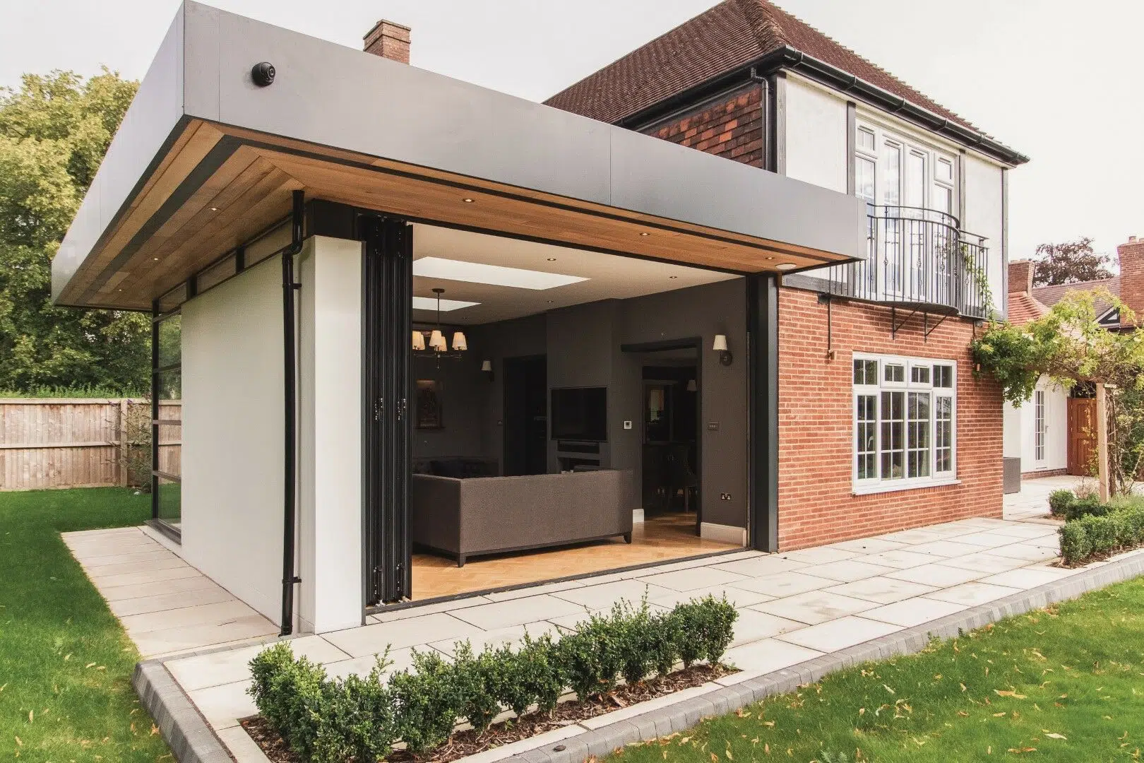 Modern brick house with a glass-walled contemporary extension opening onto a paved patio and small manicured front garden