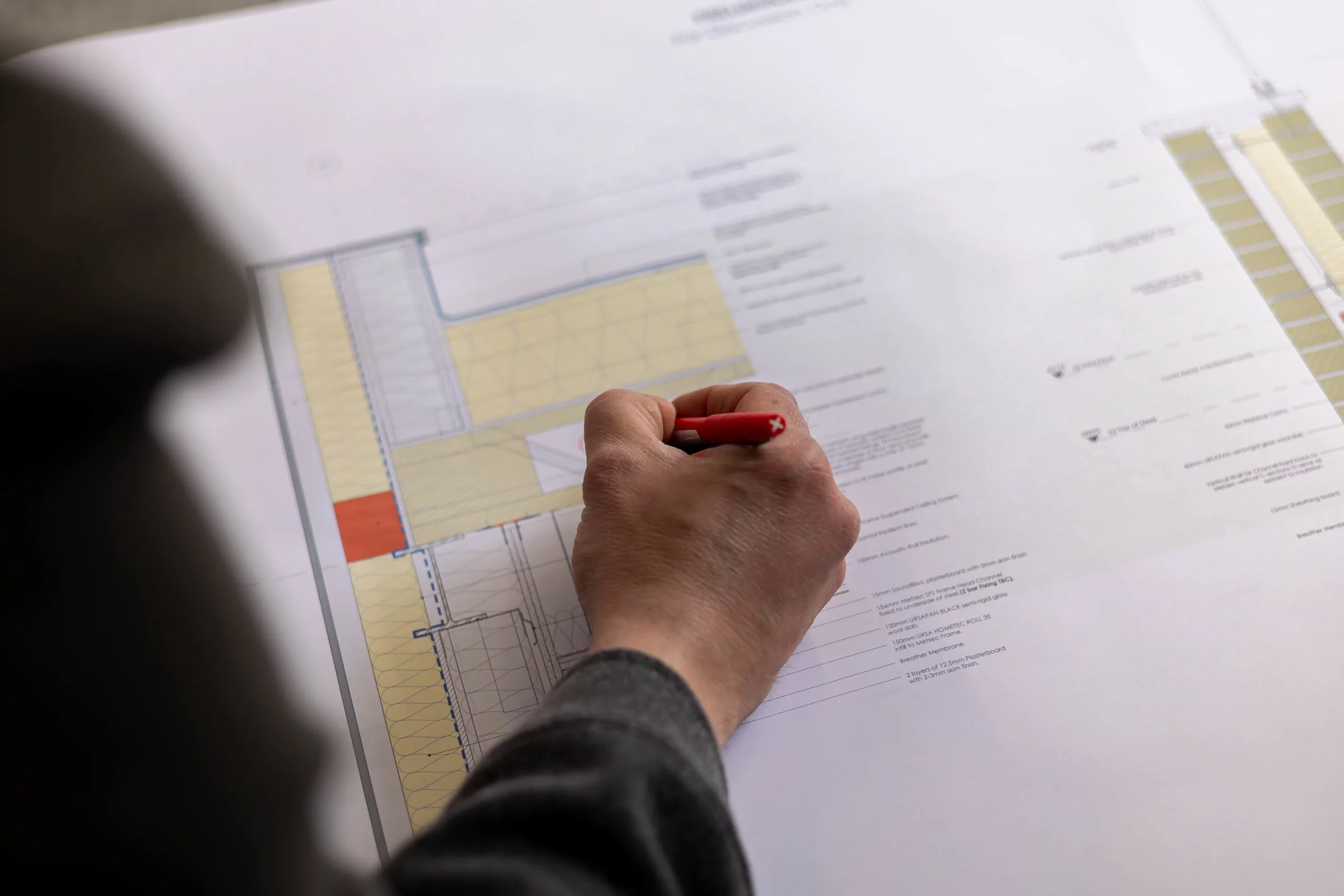Hand holding a red pen marking architectural plans and floor layout on a large printed blueprint.