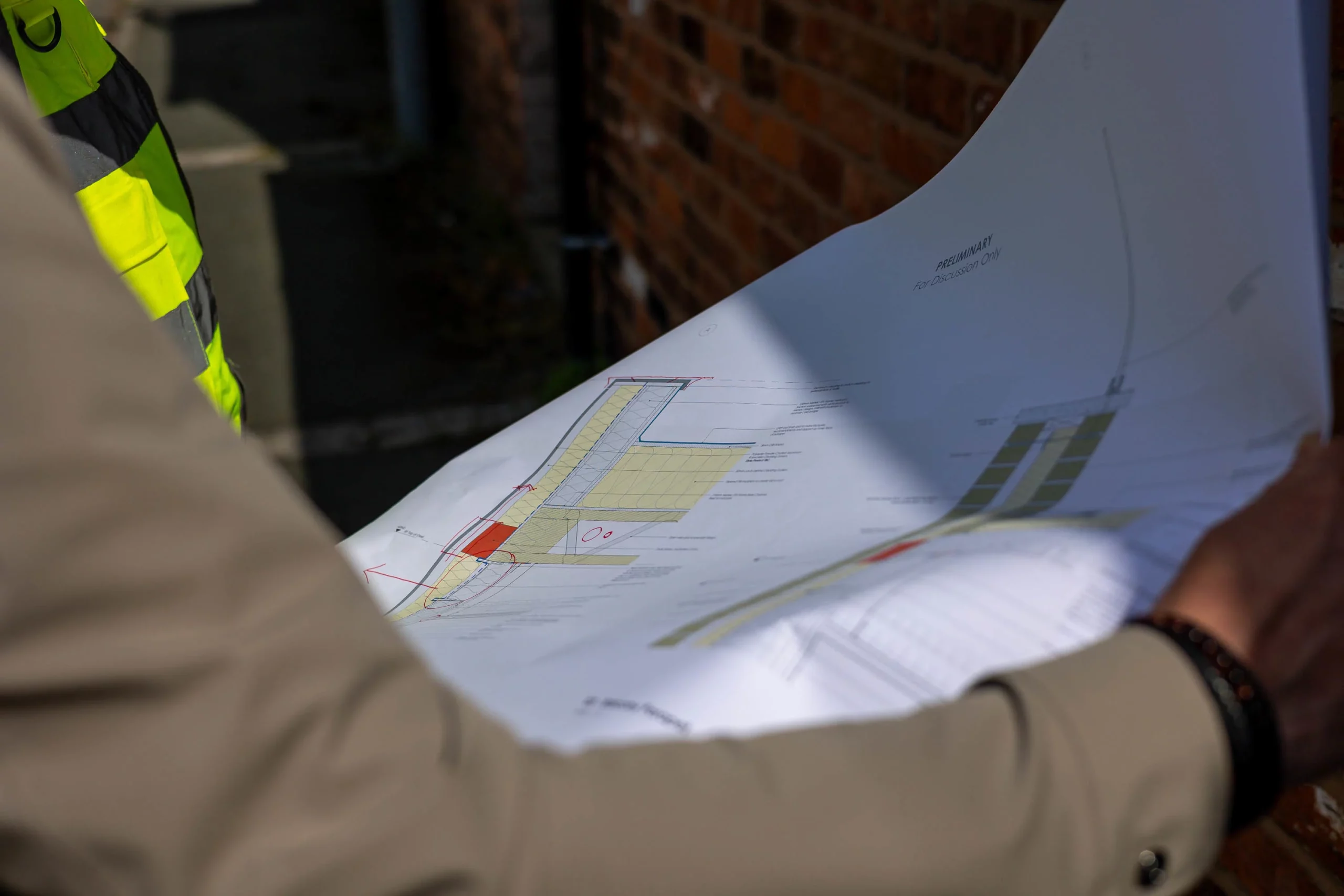 Engineer in a high-visibility vest and another person holding architectural plans with a site layout and notes visible